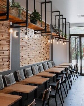 Ein modernes Restaurant mit einer langen Sitzbank, Holzverkleidungen, hängenden Pendelleuchten und Topfpflanzen.