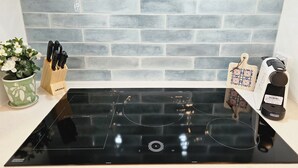 A kitchen with a black induction cooktop, a green plant, a knife block, and a coffee maker.