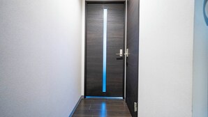 Un couloir avec une porte en bois foncé ornée d’une bande lumineuse bleue verticale.