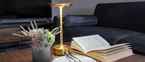A dining table with a book, a vase of flowers, and a candle.