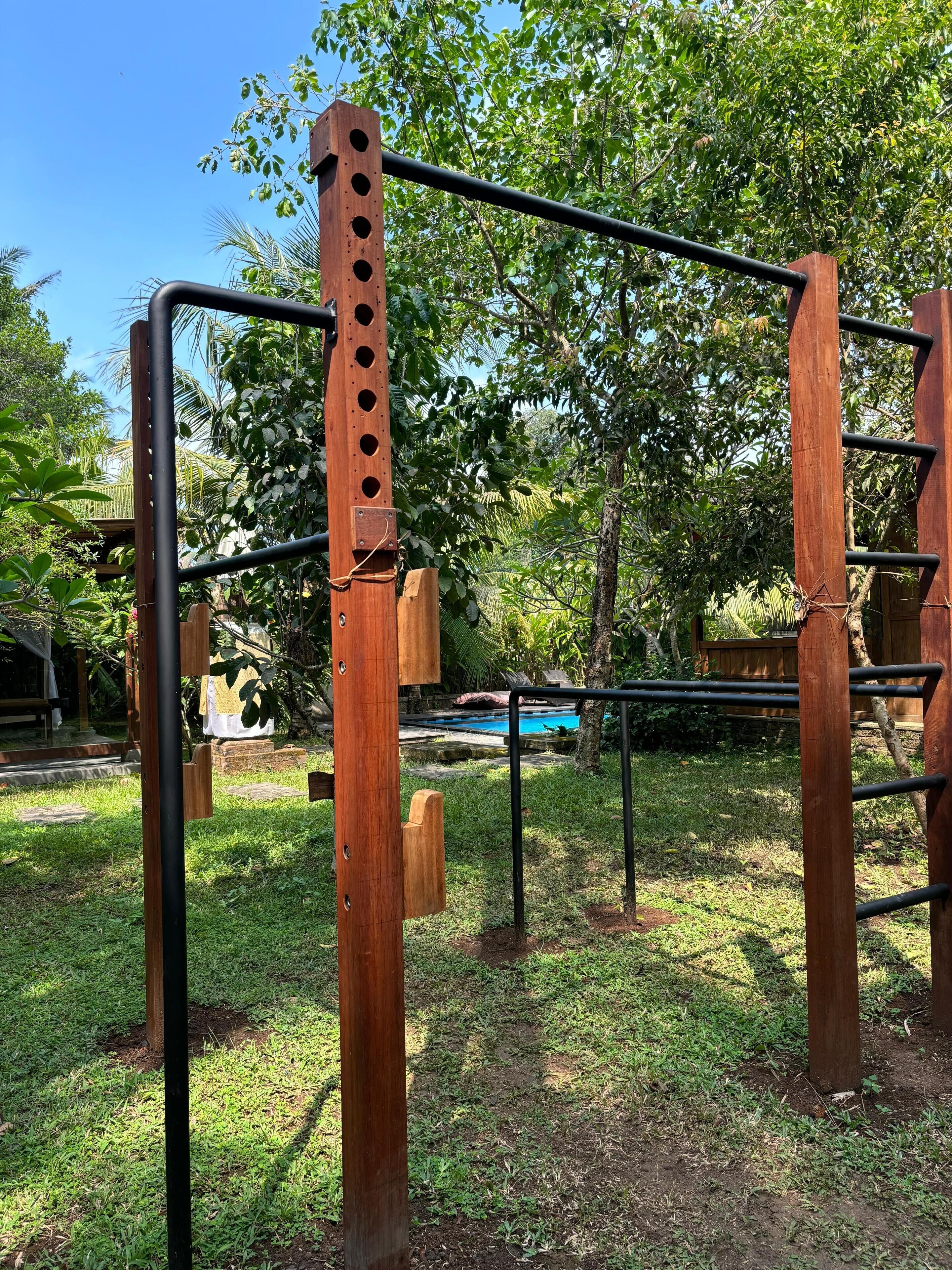 Estructura de gimnasio al aire libre de metal y madera con barra de dominadas y una escalera.