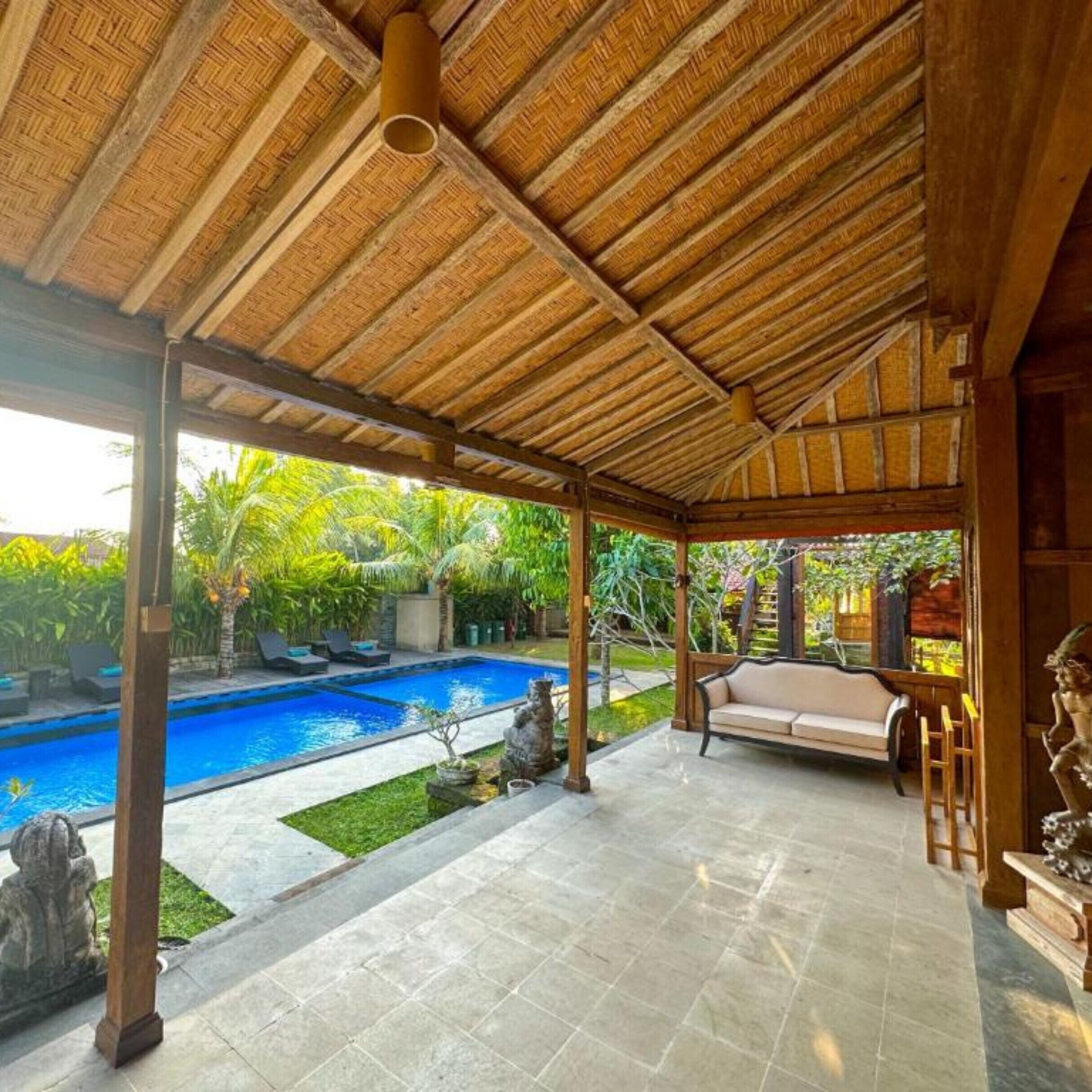 A covered outdoor area with a pool, seating, and a view of a tropical garden.