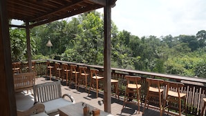 An outdoor deck with wooden furniture, including benches and a table, overlooking a lush green forest. - Nunu Bali Eco Friendly Retreat (Tabanan)