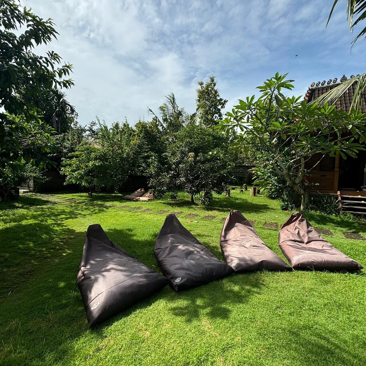 A grassy outdoor area with three bean bags and a wooden structure in the background.