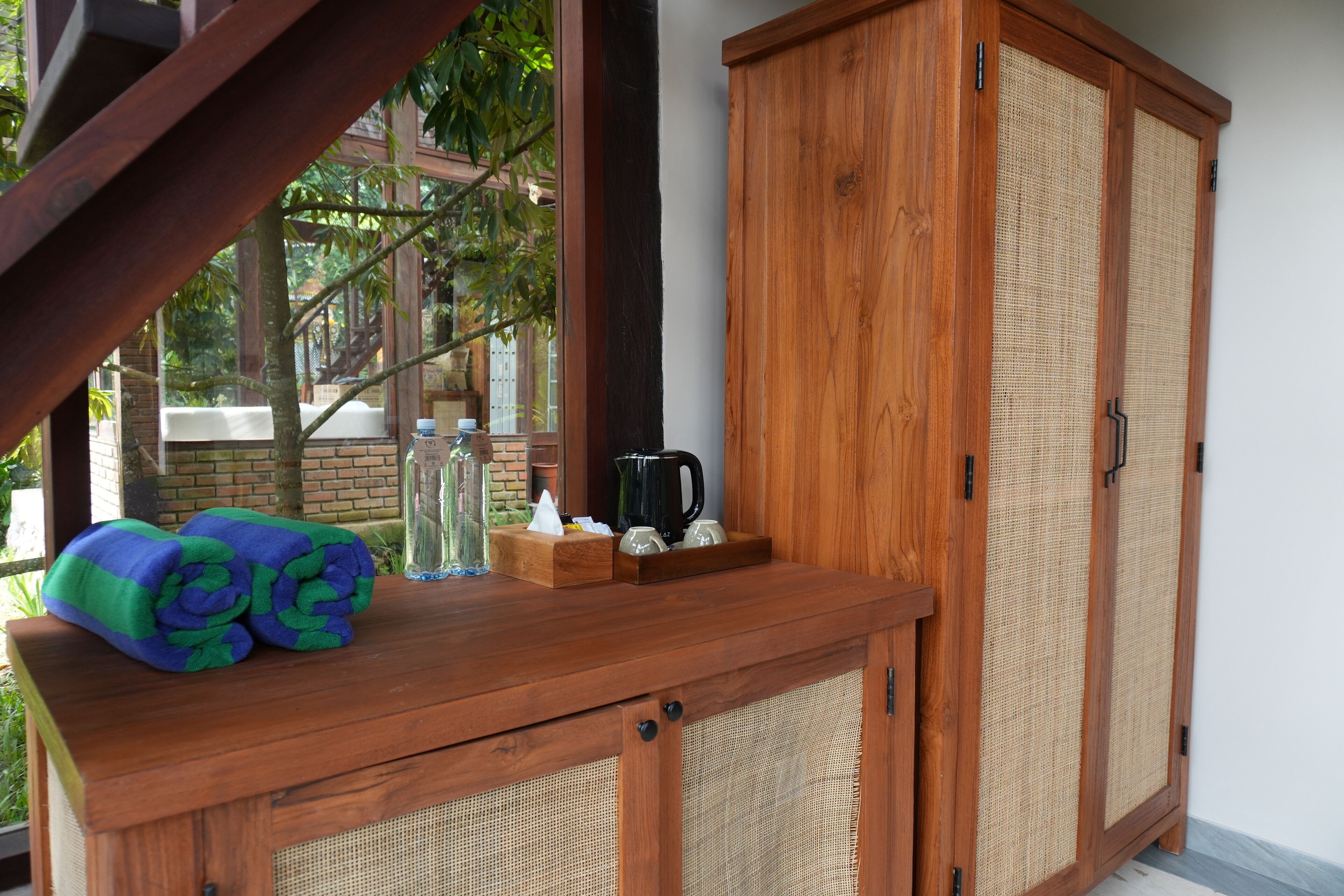 A wooden cabinet with woven panels, a glass container, and a rolled towel on a wooden table.