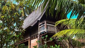 A traditional wooden building with a thatched roof, surrounded by lush greenery and palm trees. - Nunu Bali Eco Friendly Retreat (Tabanan)