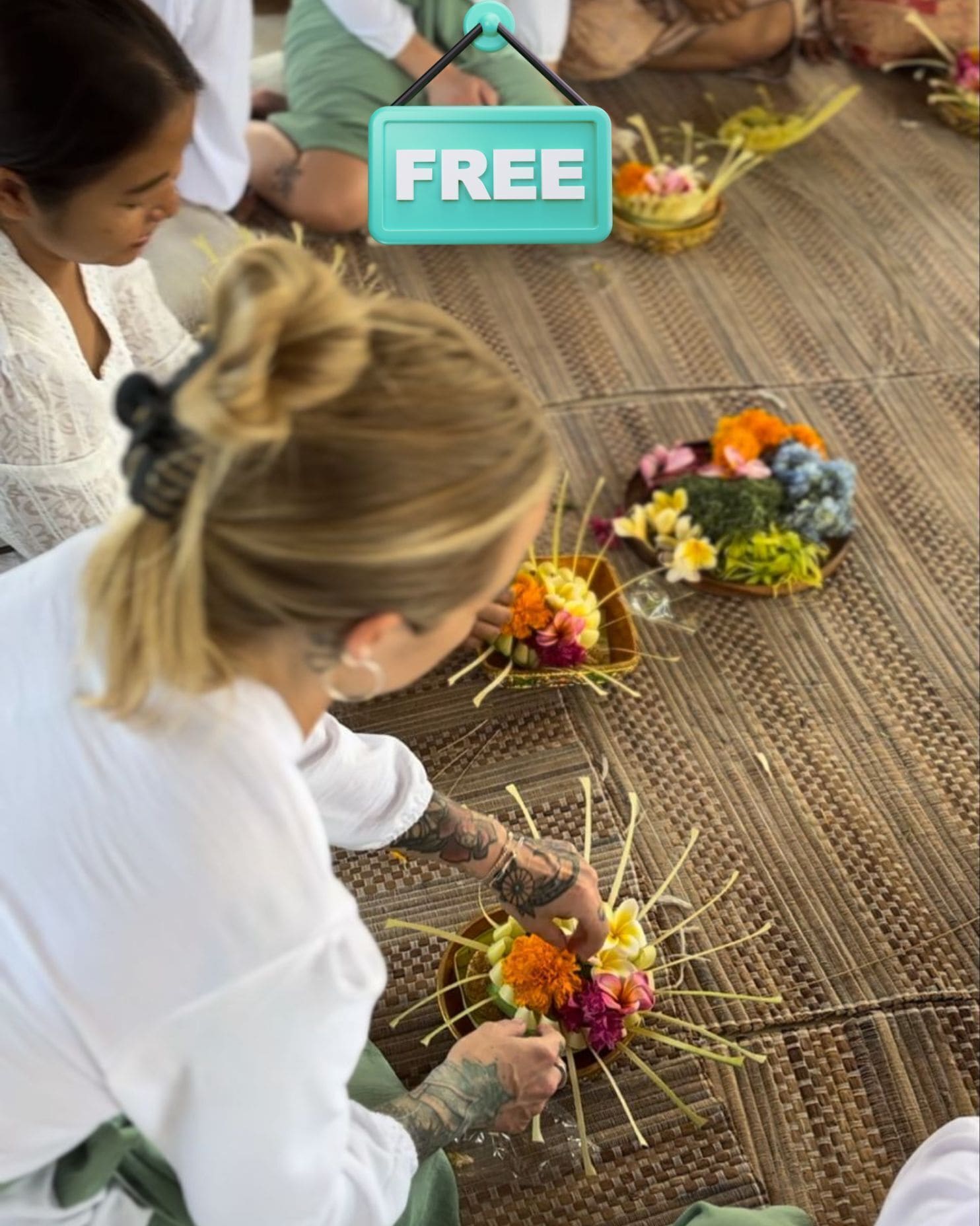A group of people sitting on a woven mat, each holding a small bowl with colorful flowers.