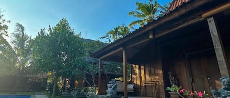 A traditional wooden building with a tiled roof, a swimming pool, and a well-maintained garden with palm trees and a bonsai tree.