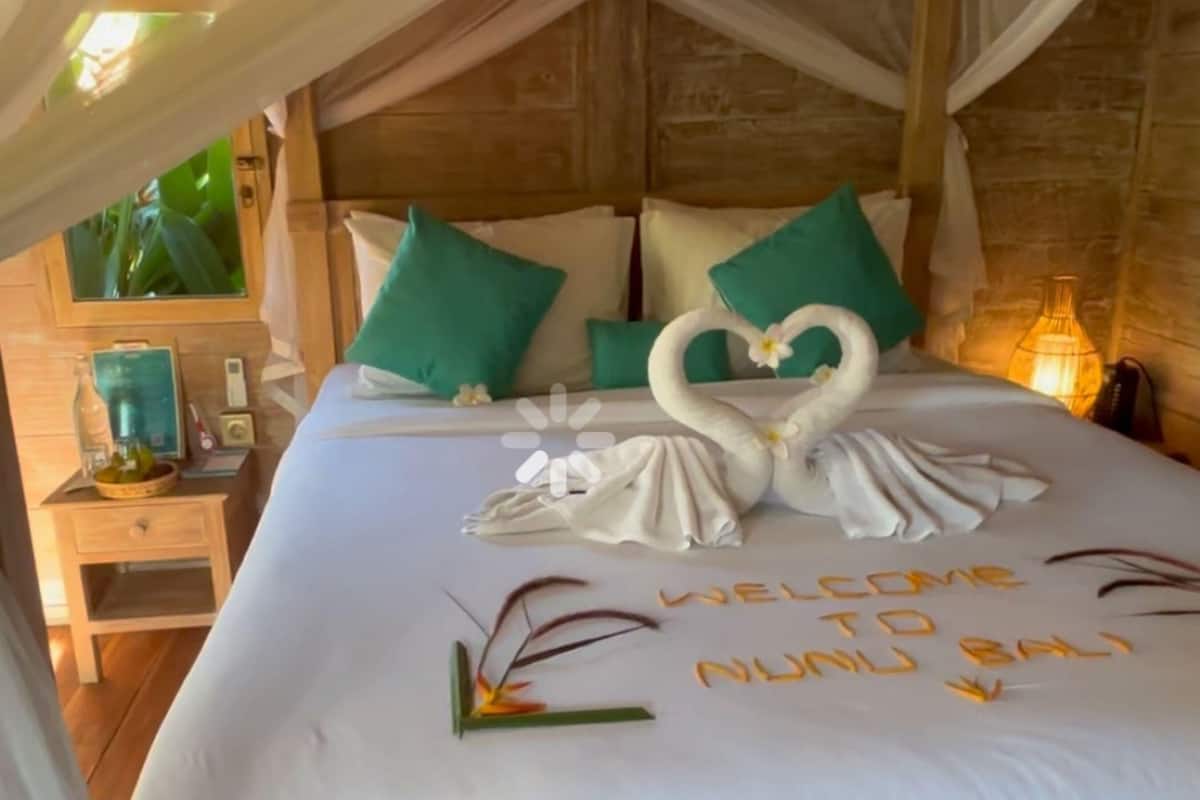 Un letto con un’elegante composizione di cuscini a forma di cigno e un cartello di benvenuto.