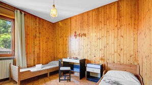A room with wooden panel walls, a bed, a desk, a chair, and a small table with a lamp. - A Due Passi Dal Bosco: Hillside Apartment with Garden&BBQ, Laveno Mombello, Italy (Laveno Mombello)