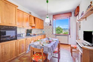 Une cuisine compacte avec des meubles en bois, une table à manger pour deux personnes et une fenêtre donnant sur un paysage verdoyant.