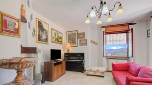 A living room with a television, a piano, a red sofa, and a window with a view. - A Due Passi Dal Bosco: Hillside Apartment with Garden&BBQ, Laveno Mombello, Italy (Laveno Mombello)