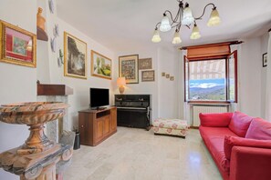 Un salon avec une télévision, un piano, un canapé rouge et une fenêtre donnant sur un beau paysage.