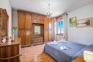 Hotelkamer met een houten kledingkast, een bed met blauw beddegoed, een kroonluchter en een raam met uitzicht.