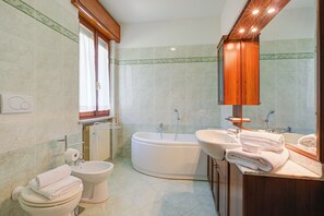 Een badkamer met toilet, bidet, badkuip en een wastafel met spiegel.