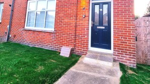 A red brick two-story residential building with a black front door, white-framed windows, and a small front garden. - Forge Lane Cozy Apartment (Gillingham)