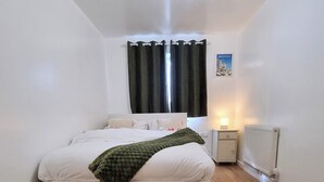 A bedroom with a bed, a nightstand, a lamp, and a radiator. - Forge Lane Cozy Apartment (Gillingham)