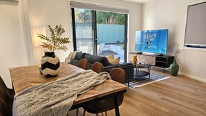 A modern living room with a wooden dining table, a sofa, and a television.