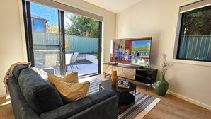A living room with a dark sofa, a coffee table, a TV, and a sliding glass door leading to an outdoor patio.