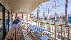 A covered deck with wooden benches and a grill, overlooking a lake with trees and buildings in the background. - Lakefront Access - Hour from DC - Kayaks Provided (Locust Grove)