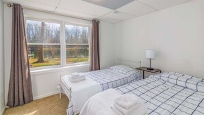 A hotel room with two beds, a window with curtains, a bedside table with a lamp, and a view of a tree and lake outside. - Lakefront Access - Hour from DC - Kayaks Provided (Locust Grove)