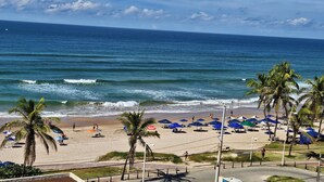 A beach with umbrellas, palm trees, and the ocean. - Beautiful beachfront penthouse, right on the sand, with a private barbecue area. (Salvador)