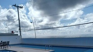 A rooftop pool area with a clear view of the ocean, a pool, and outdoor seating. - Beautiful beachfront penthouse, right on the sand, with a private barbecue area. (Salvador)