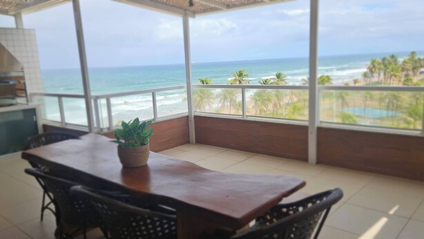 A balcony with a view of the ocean and a wooden table with chairs. - Beautiful beachfront penthouse, right on the sand, with a private barbecue area. (Salvador)