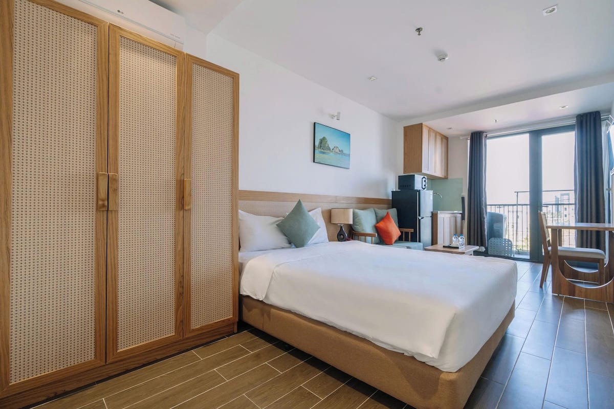 Ein Hotelzimmer mit einem großen Bett, einem Schrank, einem Schreibtisch mit Stuhl, einem Fenster und einem Balkon.