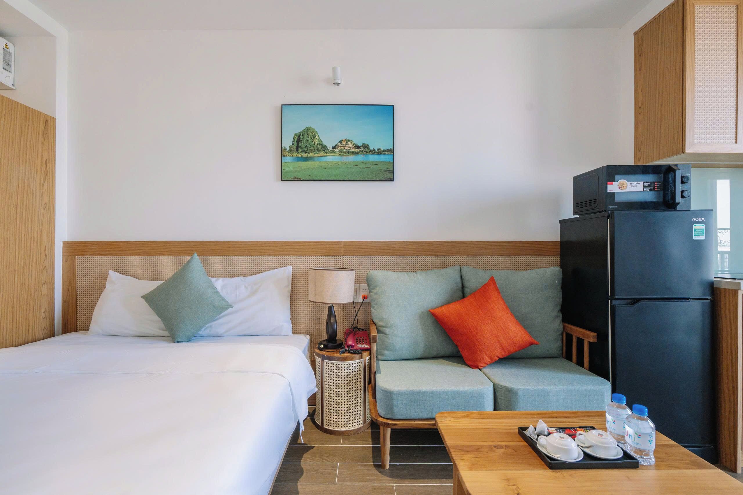 A hotel room with two beds, a sofa, a dining table, a refrigerator, and a wall-mounted picture.