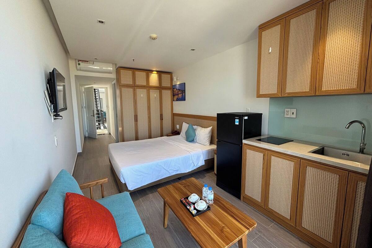 Ein Hotelzimmer mit einem Bett, einem Sofa, einem Holztisch mit Tablett, einem schwarzen Kühlschrank, einem Waschbecken und einem an der Wand befestigten Fernseher.