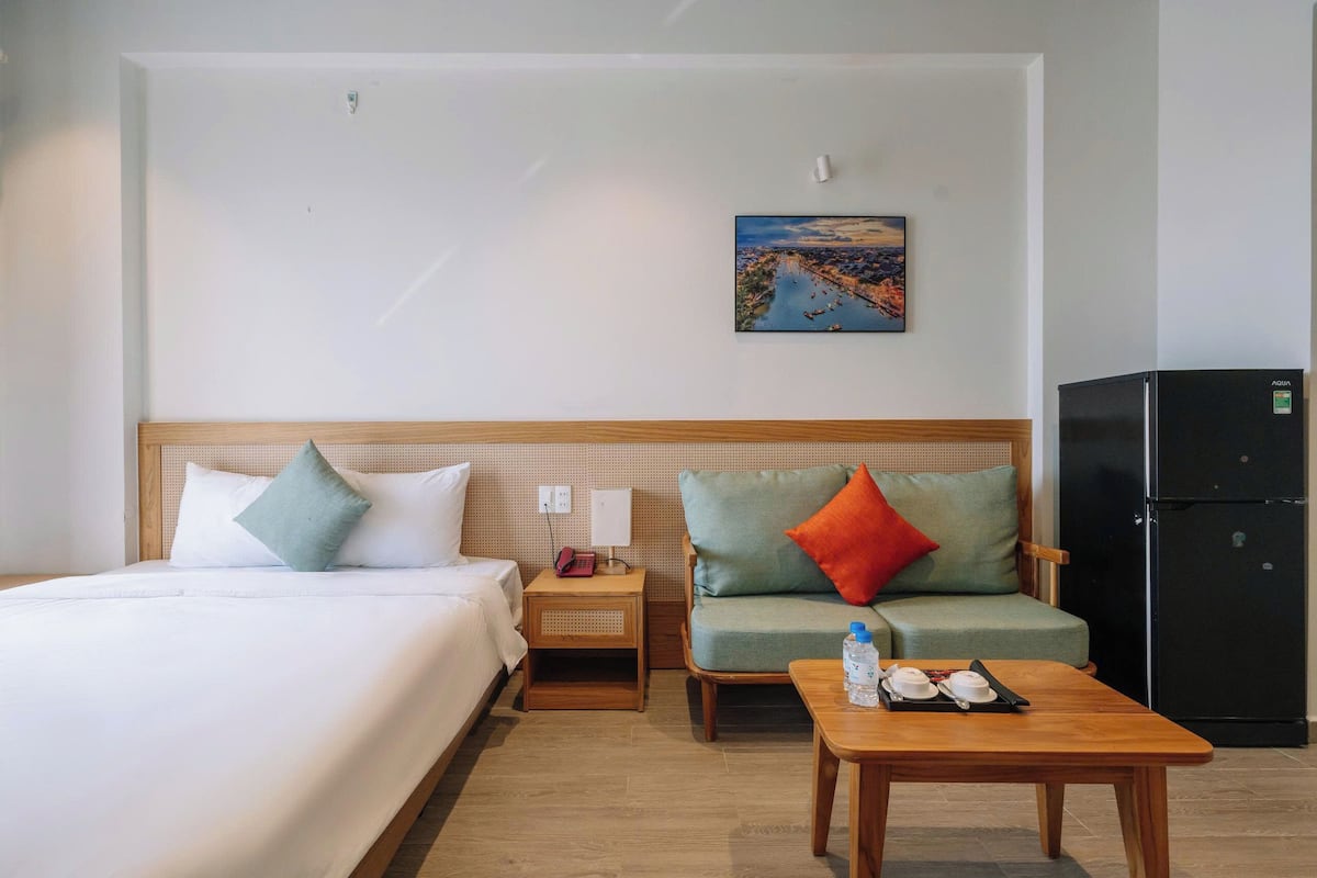 Ein Hotelzimmer mit einem Bett, einem Sofa, einem kleinen Tisch, einem Nachttisch, einem Wandbild und einem Kühlschrank.