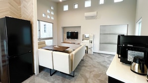 Quarto de hotel moderno com cozinha compacta, televisão de tela plana, sofá e mesa de jantar.