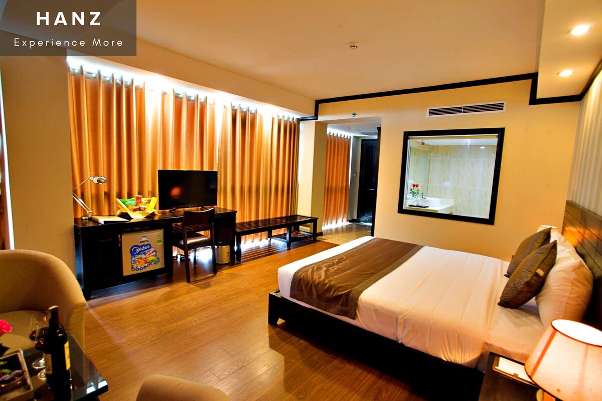 A hotel room with a bed, desk, chair, TV, and curtains.