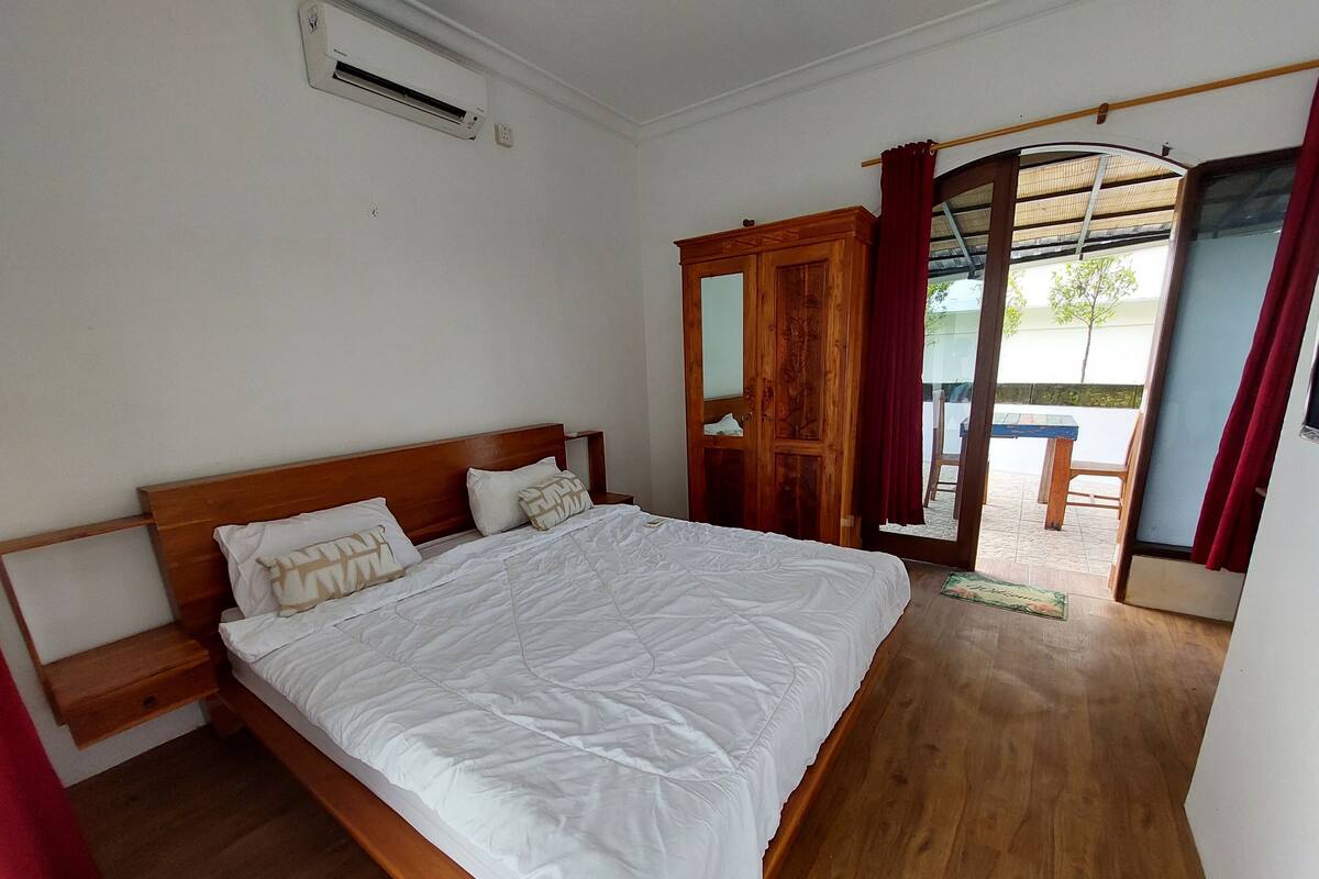 A bedroom with a wooden bed, a nightstand, a wardrobe, and a sliding glass door leading to an outdoor area.