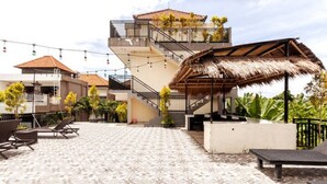 Terraço no telhado com piso de azulejos, cadeiras de descanso, estrutura de telhado de palha e escada que leva a um andar superior.