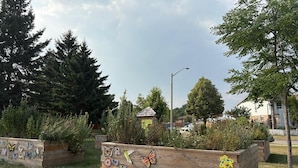 Een tuin met houten plantenbakken, decoratieve vlinders en een gebouw op de achtergrond.
