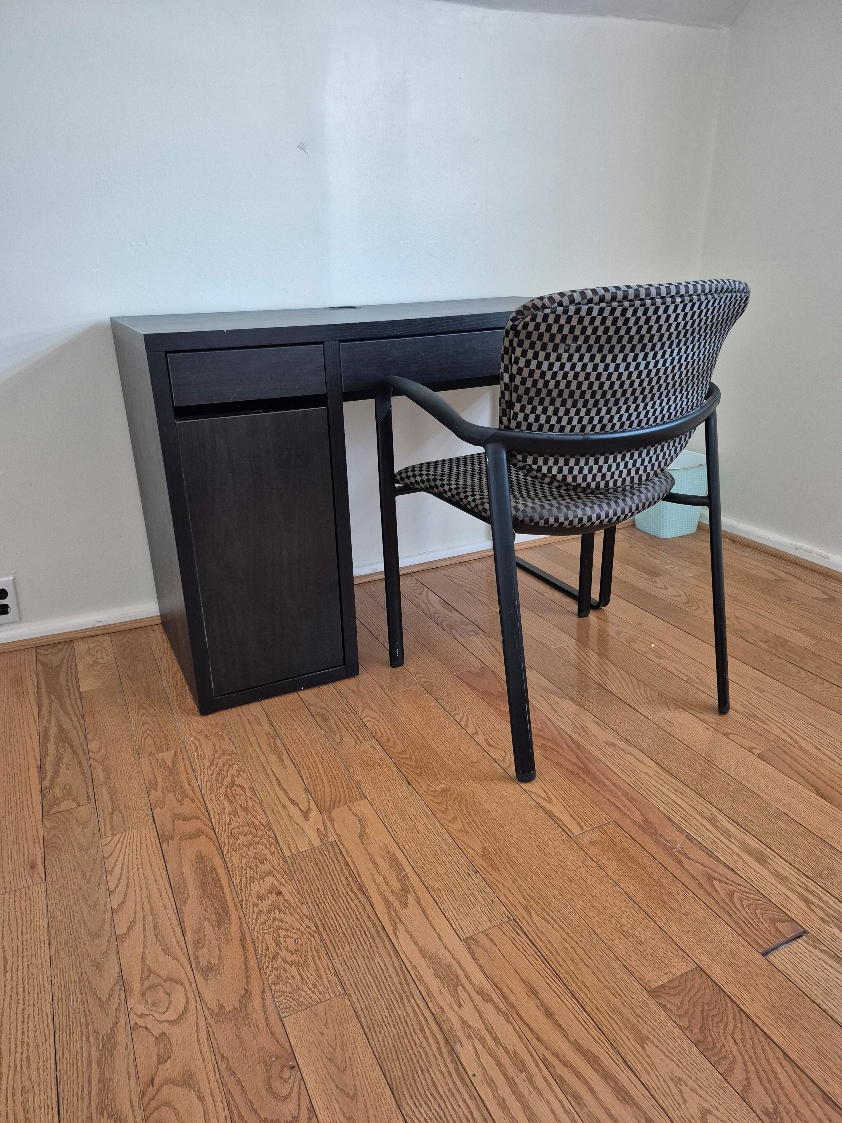 Een bureau in de hoek met een stoel, een klein kastje en een houten vloer.