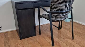 Een bureau in de hoek met een stoel, een klein kastje en een houten vloer.