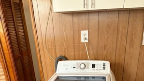 Een wasmachine en droger in witte uitvoering, met een bedieningspaneel, in een ruimte met houten wanden en een houten vloer.