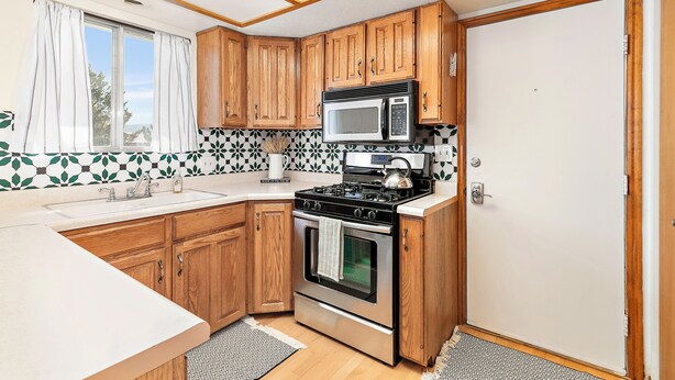A compact kitchen with wooden cabinets, a microwave, a stove, and a sink. - Quaint Swiss Chalet • Steps from Main St- Sleeps 5 (Midway)