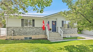 A single-story house with a brick foundation, a front porch with steps, and a small front yard. - Quaint Swiss Chalet • Steps from Main St- Sleeps 5 (Midway)