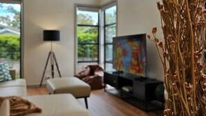 Un salon moderne comprenant un canapé, une table basse, un téléviseur et une grande fenêtre donnant sur un paysage verdoyant.