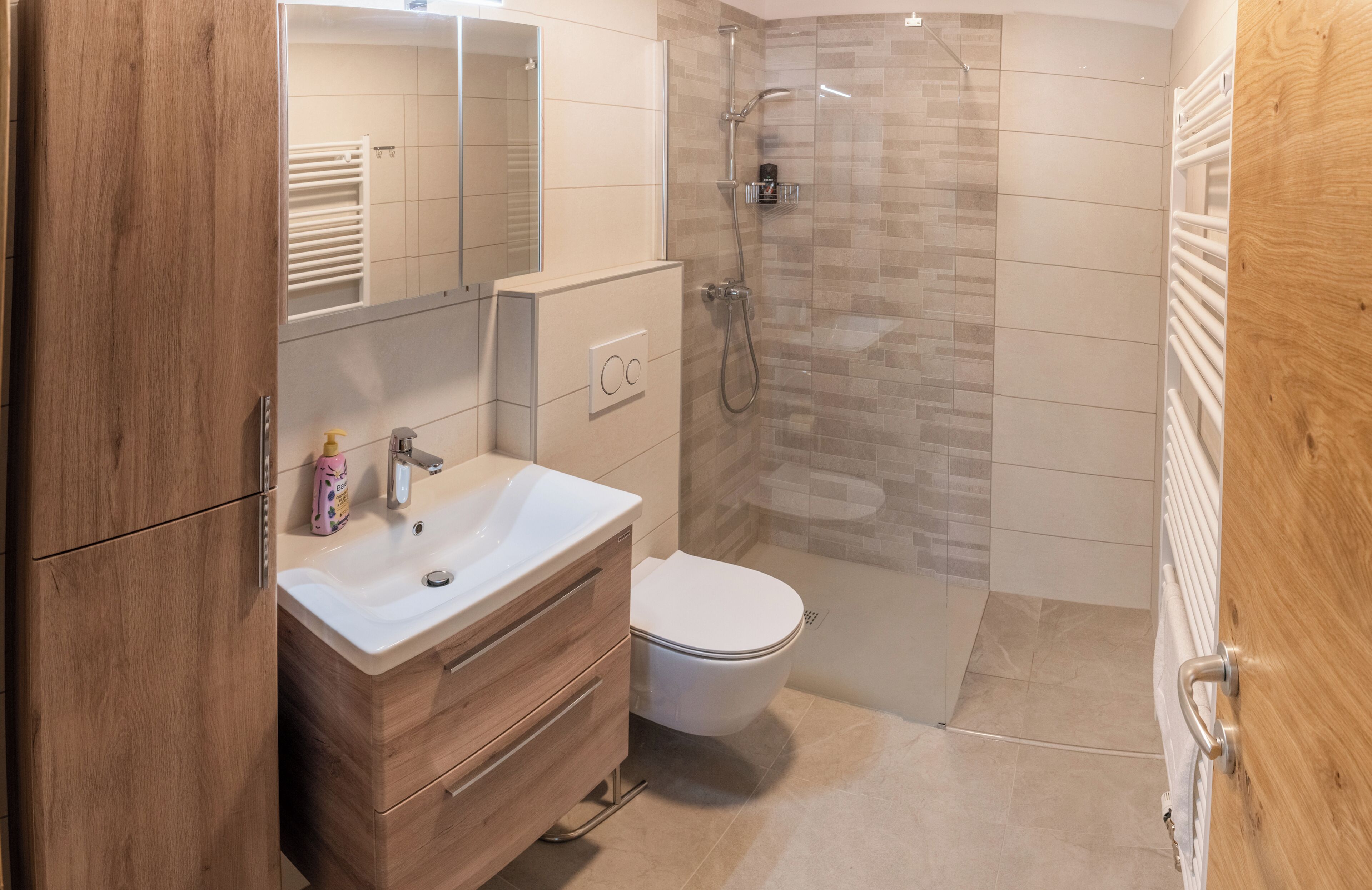 Une salle de bain moderne avec un meuble-lavabo en bois, un lavabo blanc, des toilettes et une douche séparée par une paroi en verre.