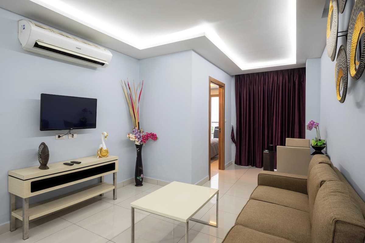A modern living room with a flat-screen TV, a beige sofa, a coffee table, a TV stand, and a decorative vase with flowers.