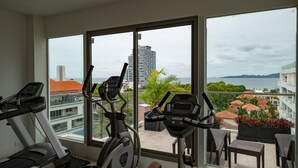 A balcony with exercise equipment and a view of buildings and a body of water. - C-View Boutique (Pattaya)