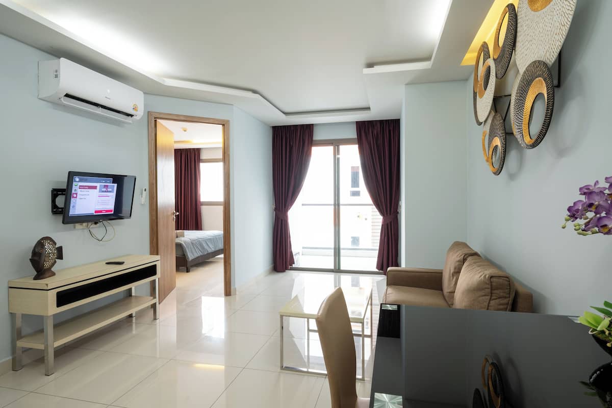 A modern living room with a flat-screen TV, a sofa, a dining table, and a large window with curtains.