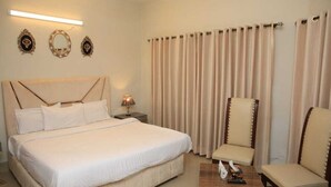 A hotel room with a large bed, two chairs, a small table with a tissue box, and a nightstand with a lamp. - Travel Lodge Islamabad F-8 (Islamabad)