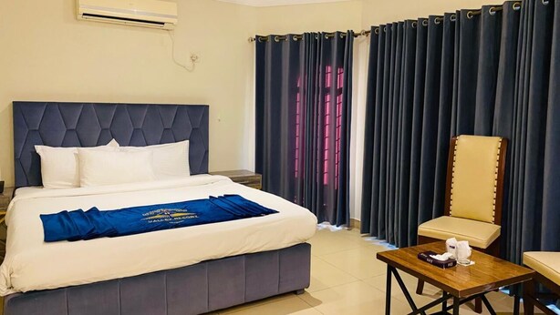 A hotel room with a large bed, a chair, a small table, and a curtain. - Travel Lodge Islamabad F-8 (Islamabad)
