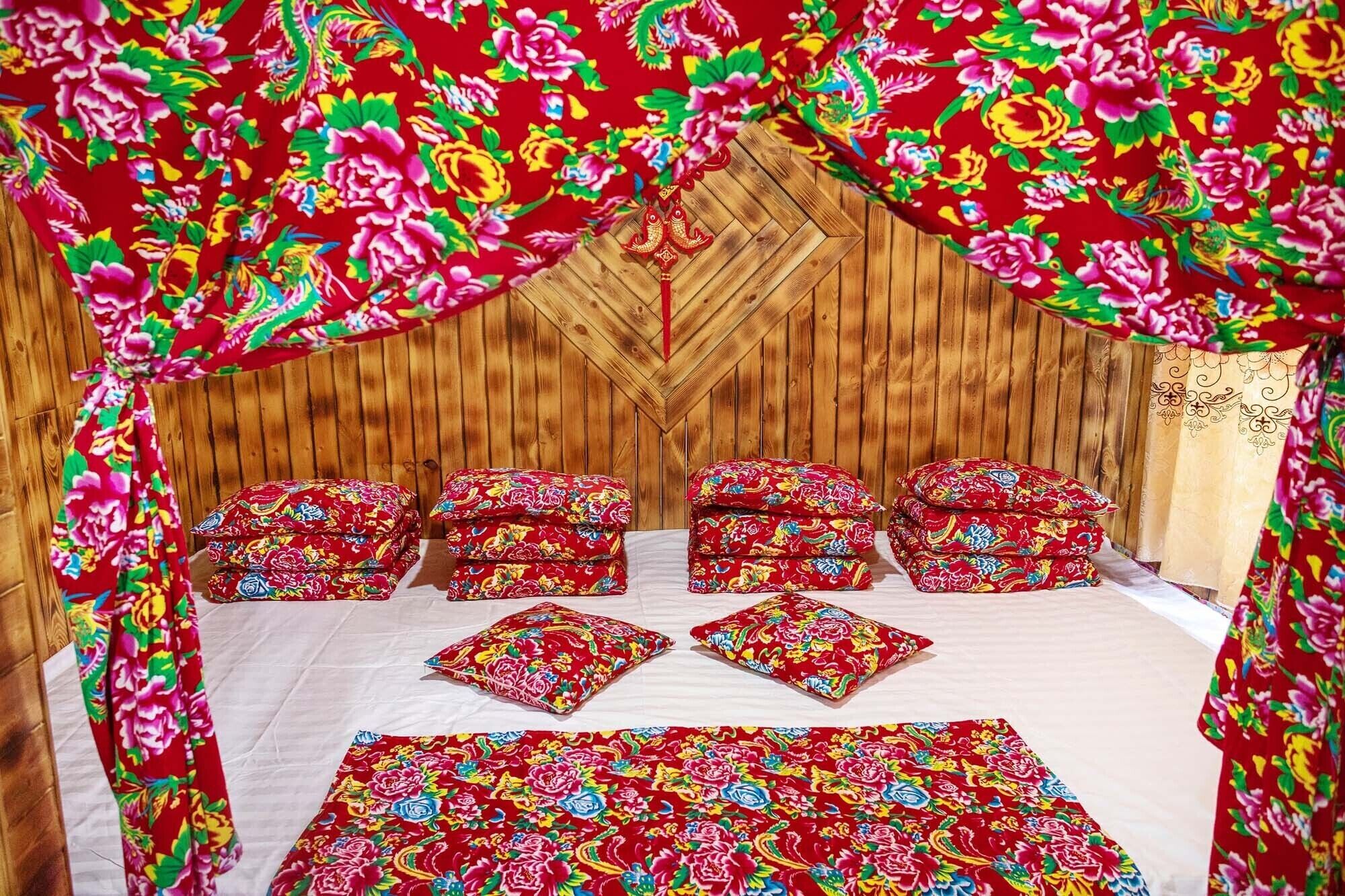 A bed with floral-patterned bedding and pillows, a wooden headboard, and a wooden wall.